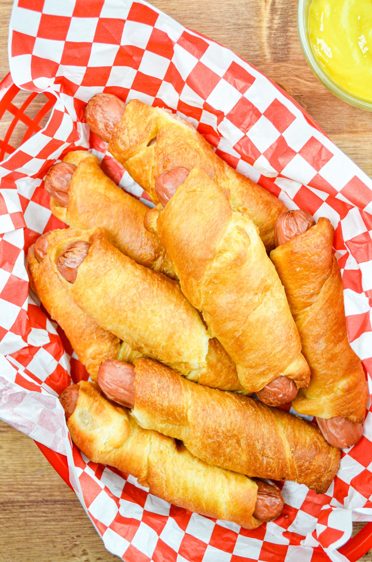 A basket full of pigs in a blanket, with mustard on the side.