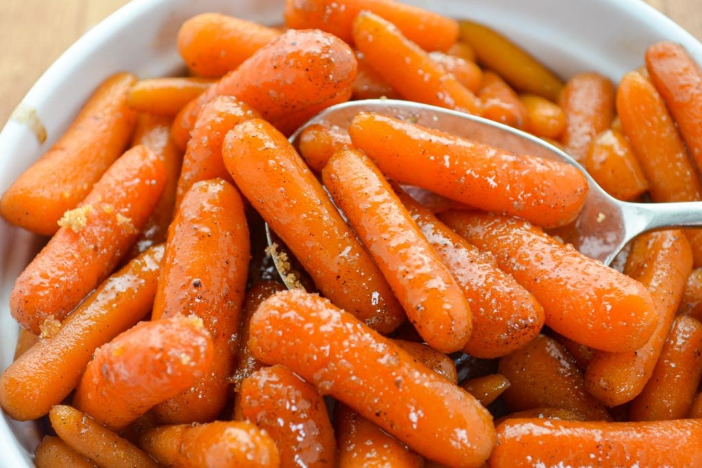 A baking dish filled with glazed baby carrots, sprinkled with brown sugar.