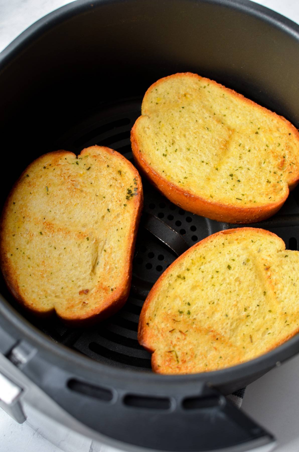 Browned and toasted garlic bread slices in the basket of an air fryer.