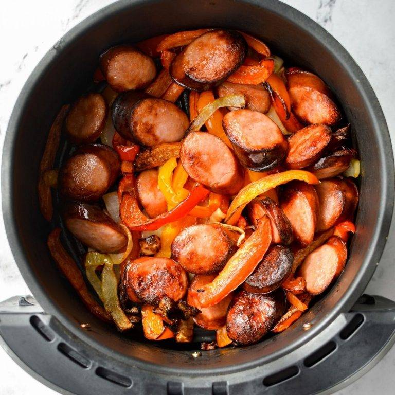 An air fryer basket, filled with cooked sausage, peppers, and onions.