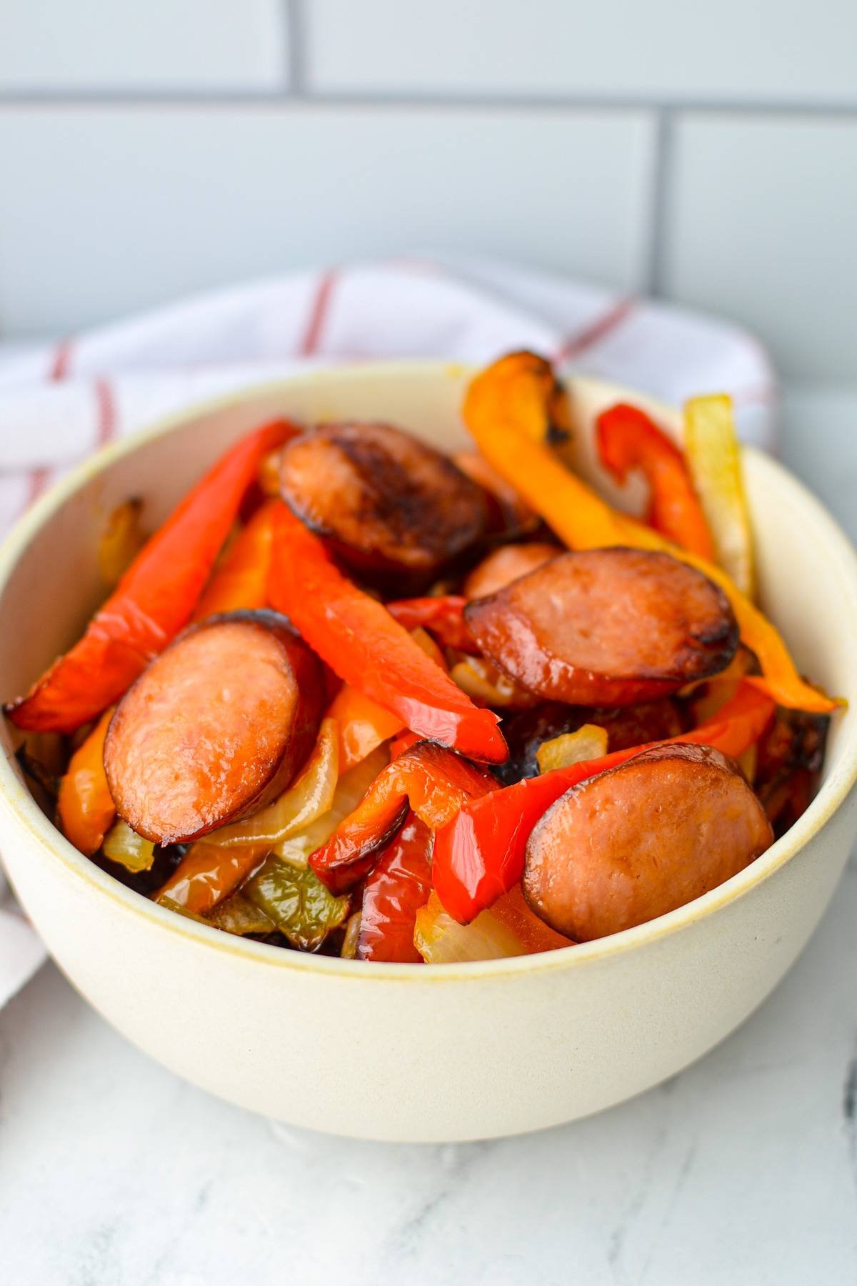 A bowl of sausage and peppers, with a white and red stripe napkin in the background.