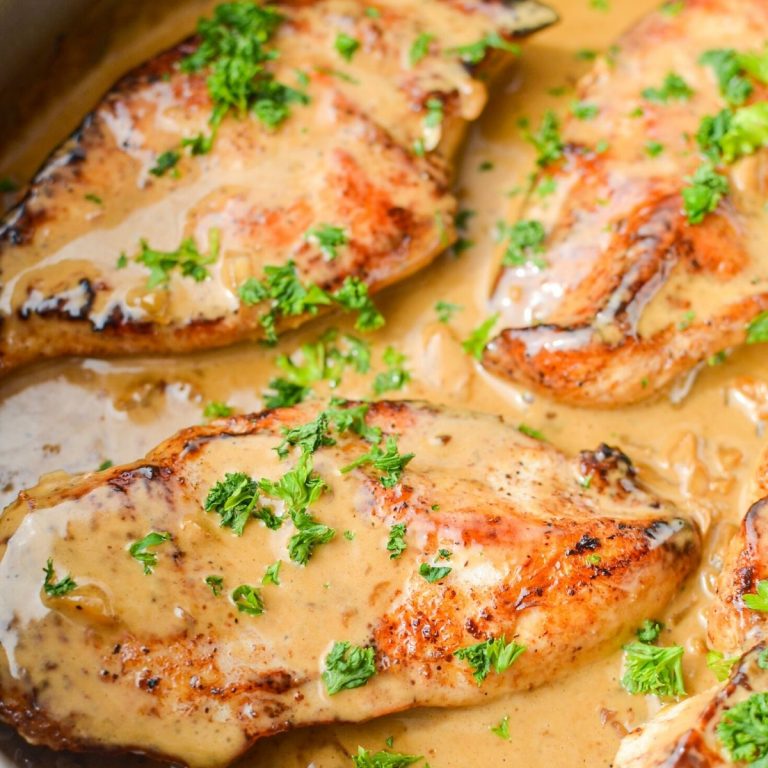 A close up of a skillet of chicken breasts in a creamy sauce, garnished with parsley.