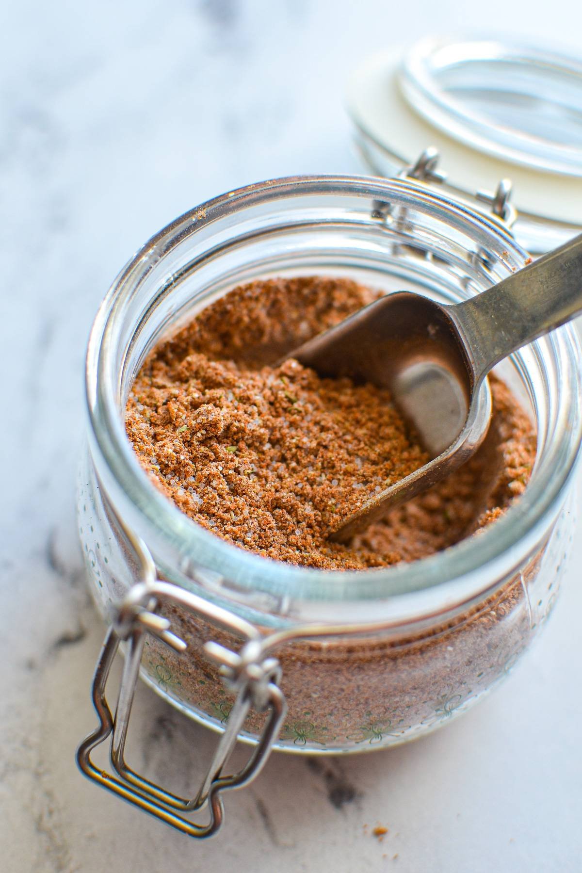 A small jar of taco seasoning with a measuring spoon inside.