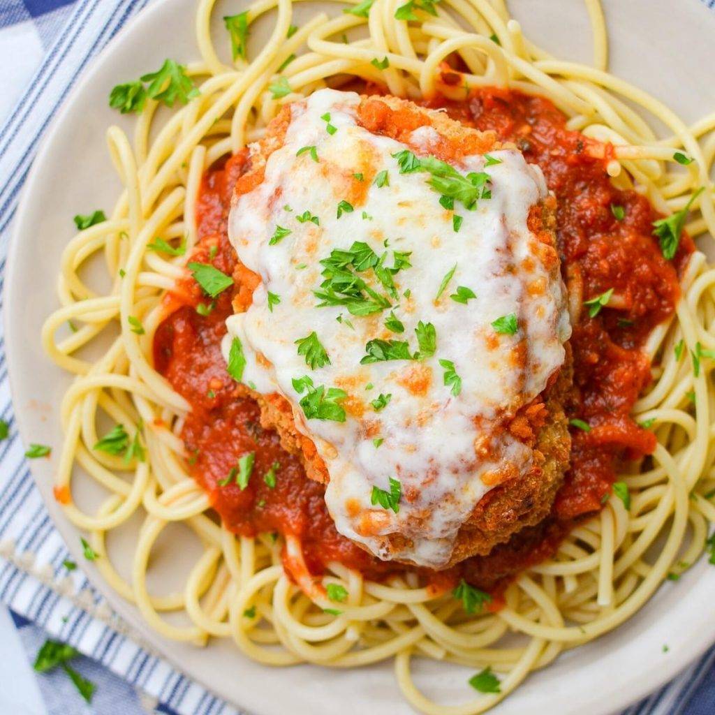 A plate of spaghetti topped with marinara sauce and a cutlet of chicken parmesan.