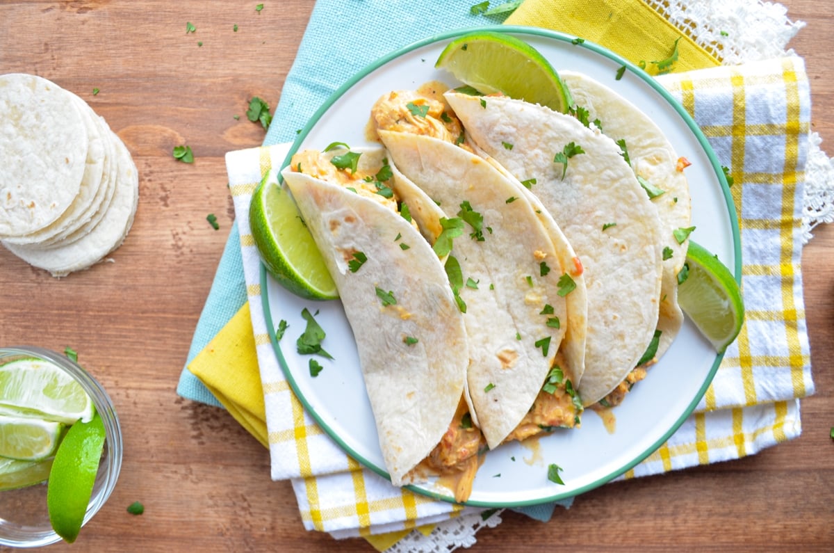 Three chicken queso tacos on a plate, resting on bright napkins.