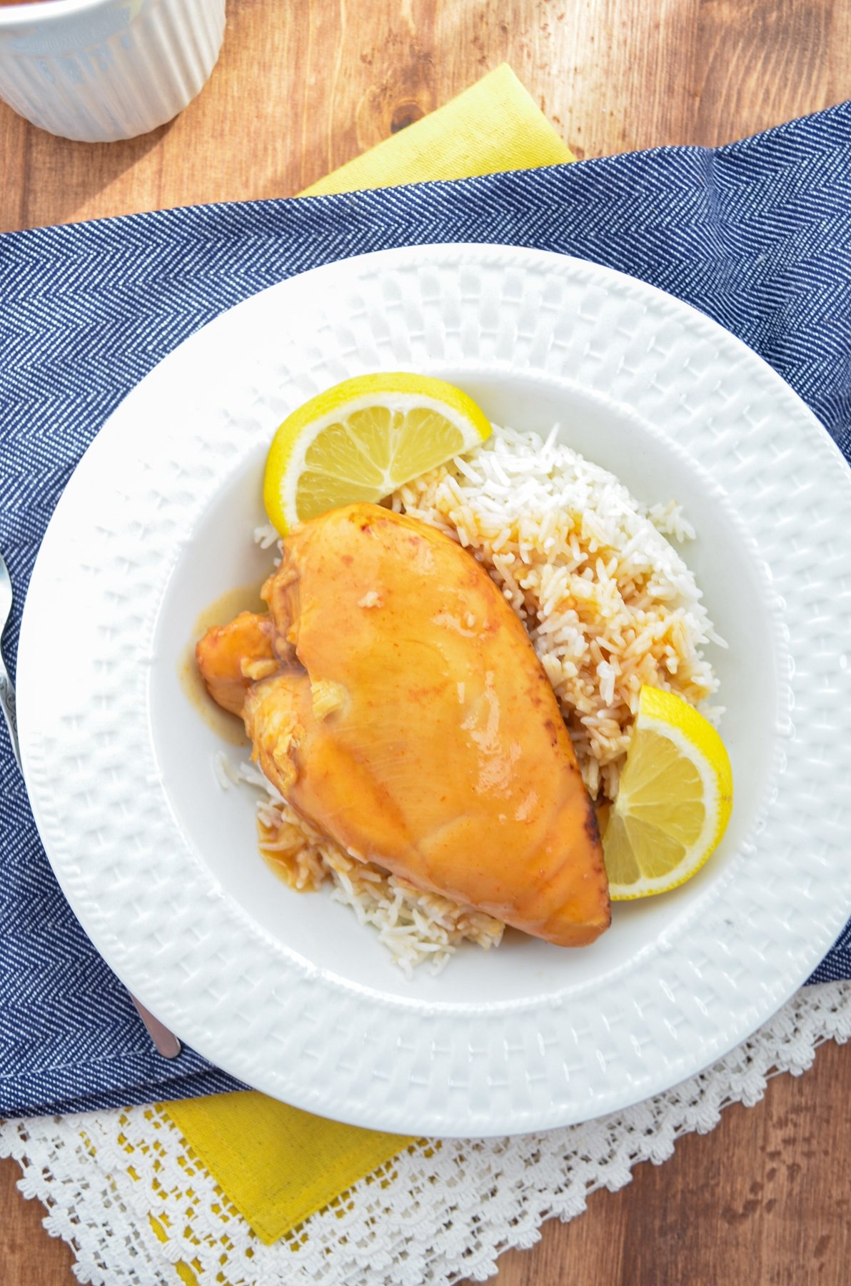 Slow cooker lemonade chicken served over rice with lemon wedges.