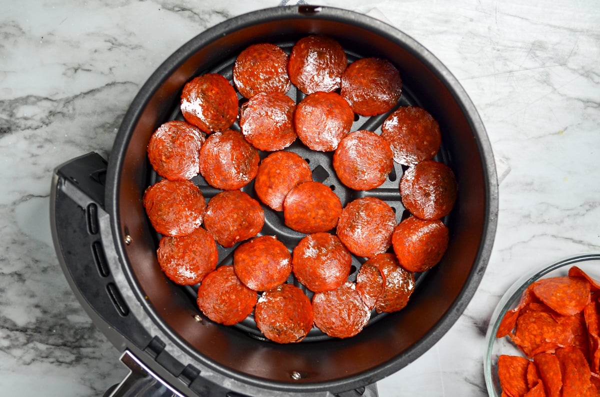 Pepperoni layered in the basket of an air fryer.