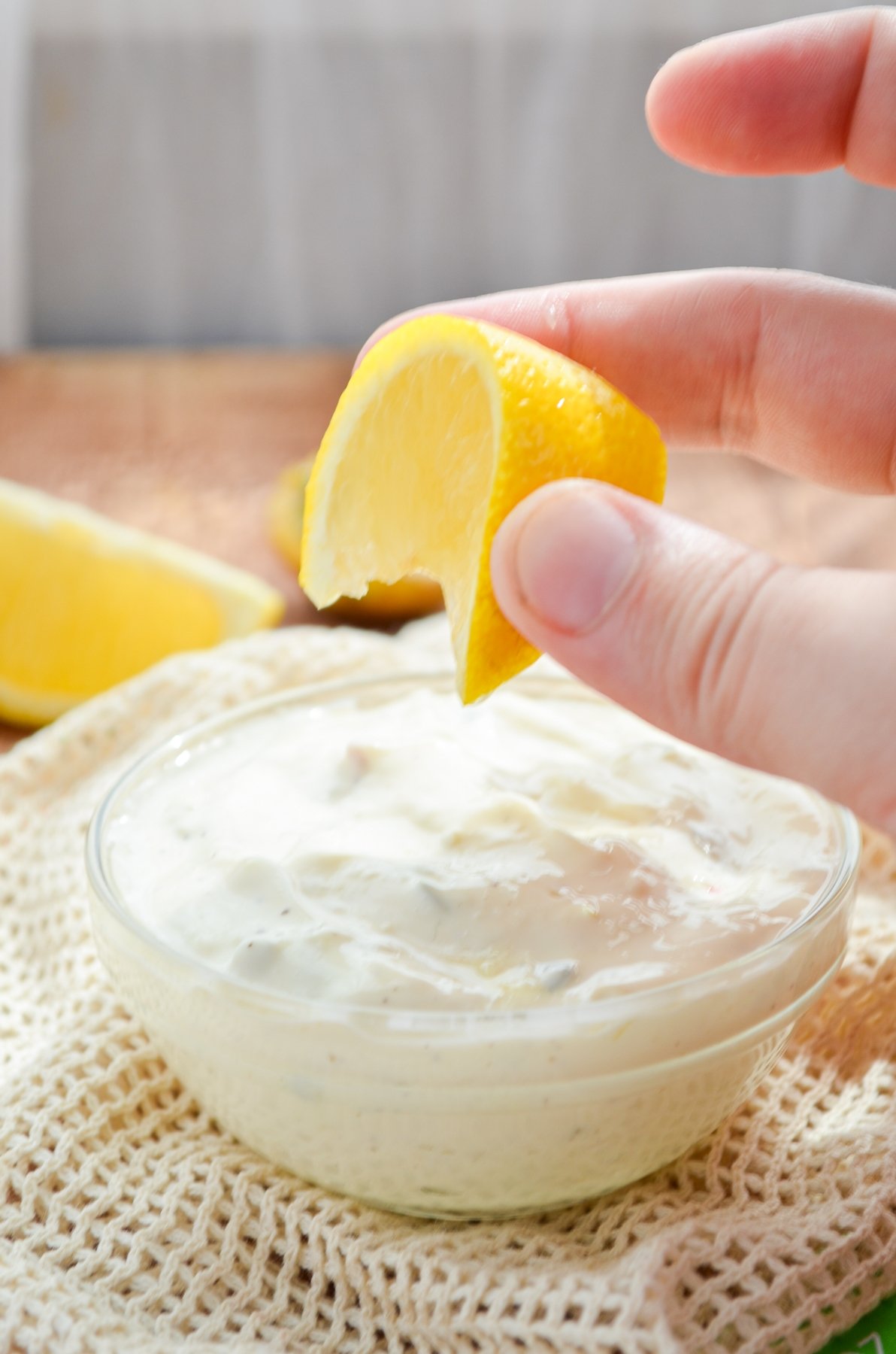 A small bowl of simple tartar sauce, with lemon being squeezed into it.