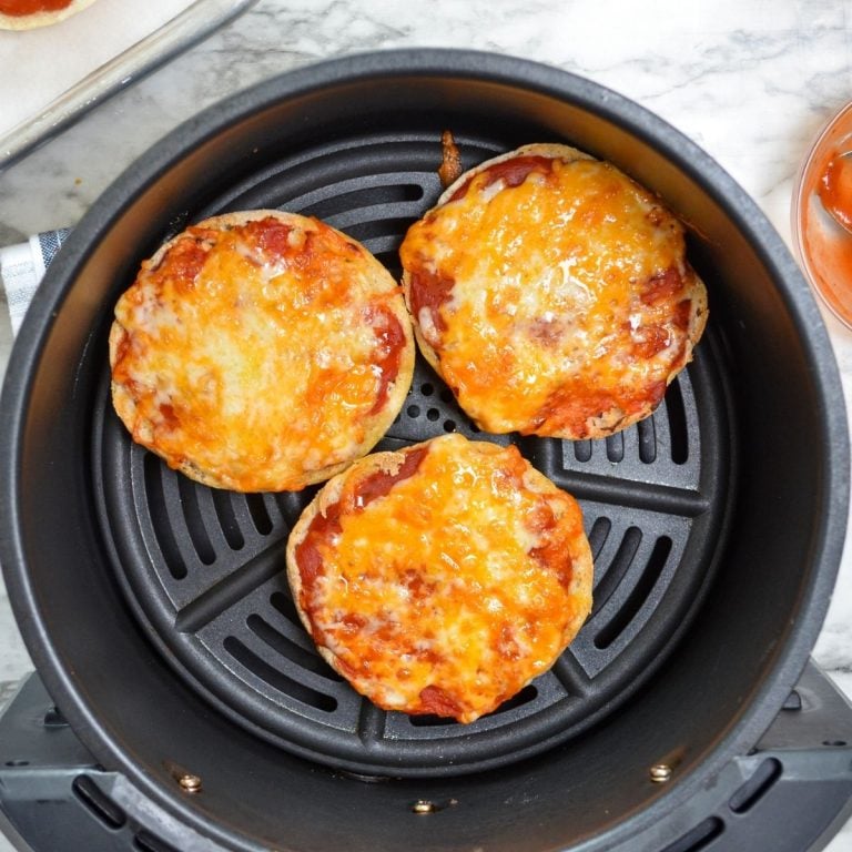 An air fryer with english muffin pizzas in the basket.