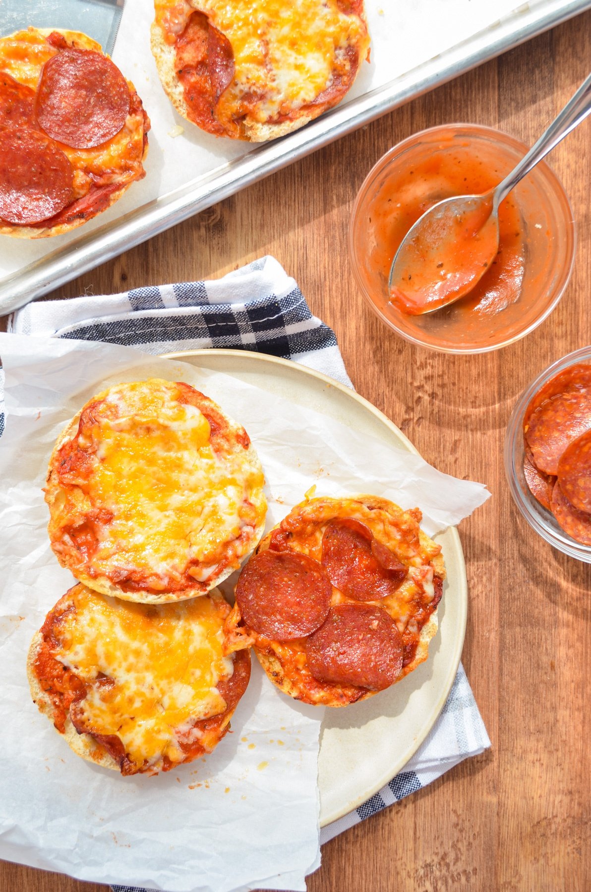 English muffin pizzas on a plate, with pizza sauce on the side.