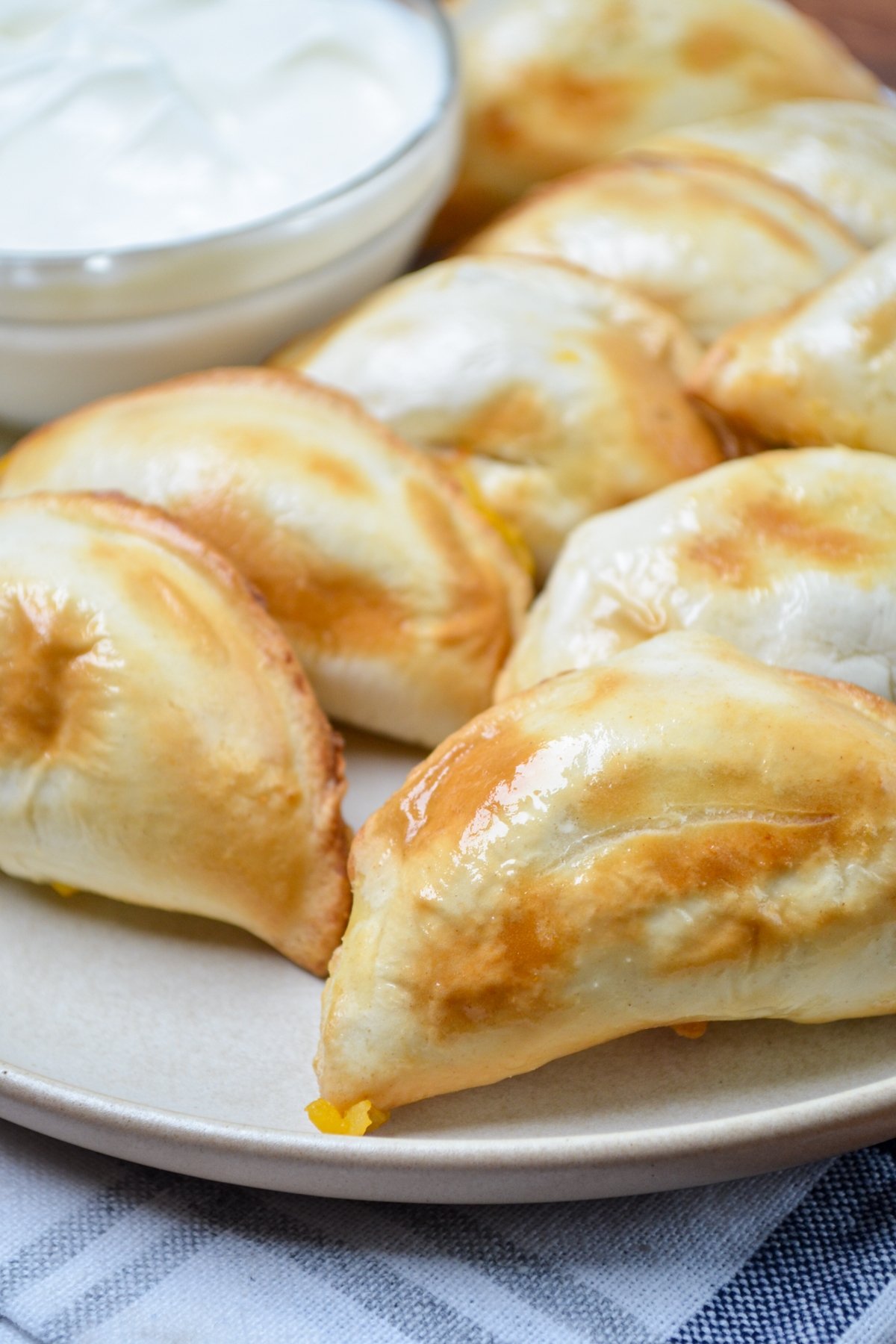 A plate of pierogies, with sour cream in the background.