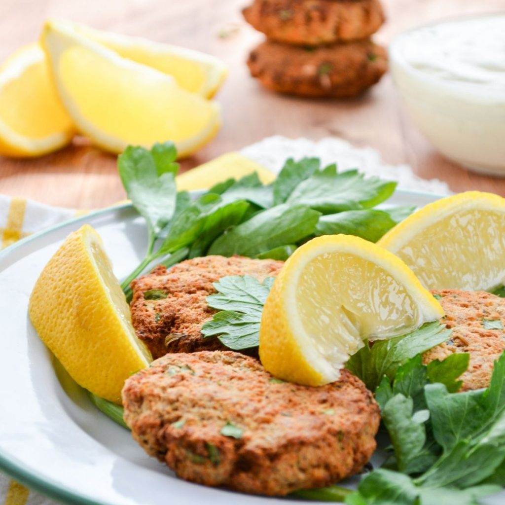 Salmon patties on a plate, garnished with parsley and lemon.