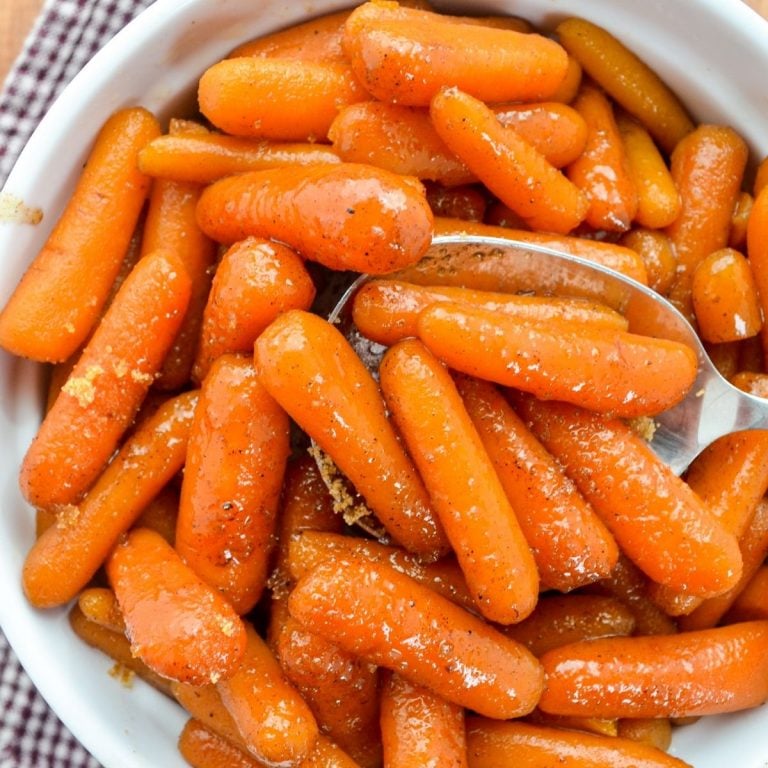 A bowl of maple glazed carrots, with a large serving spoon taking a portion out.