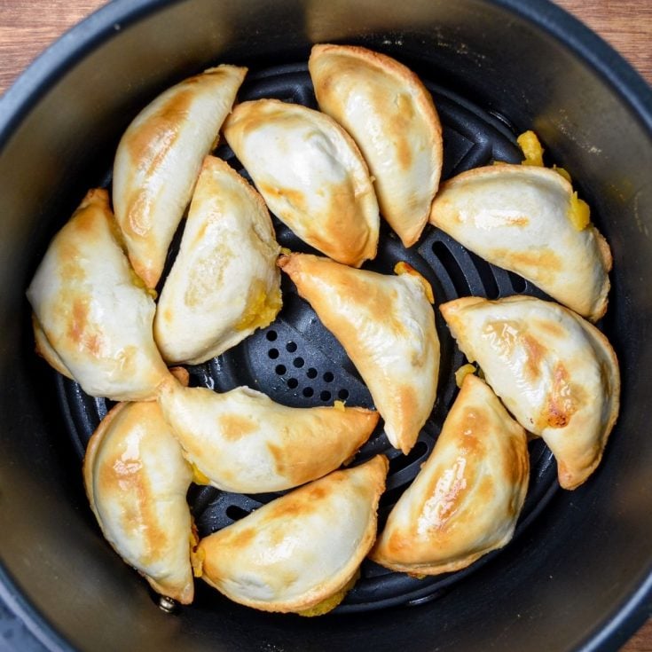 An air fryer basket, with cooked frozen pierogies.