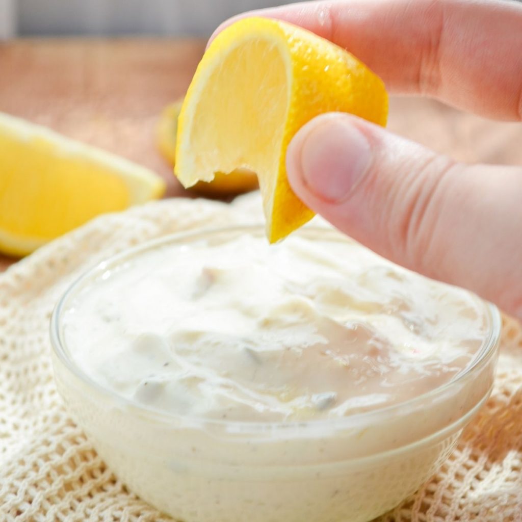 A small dish of tartar sauce, being topped with a squeeze of lemon.
