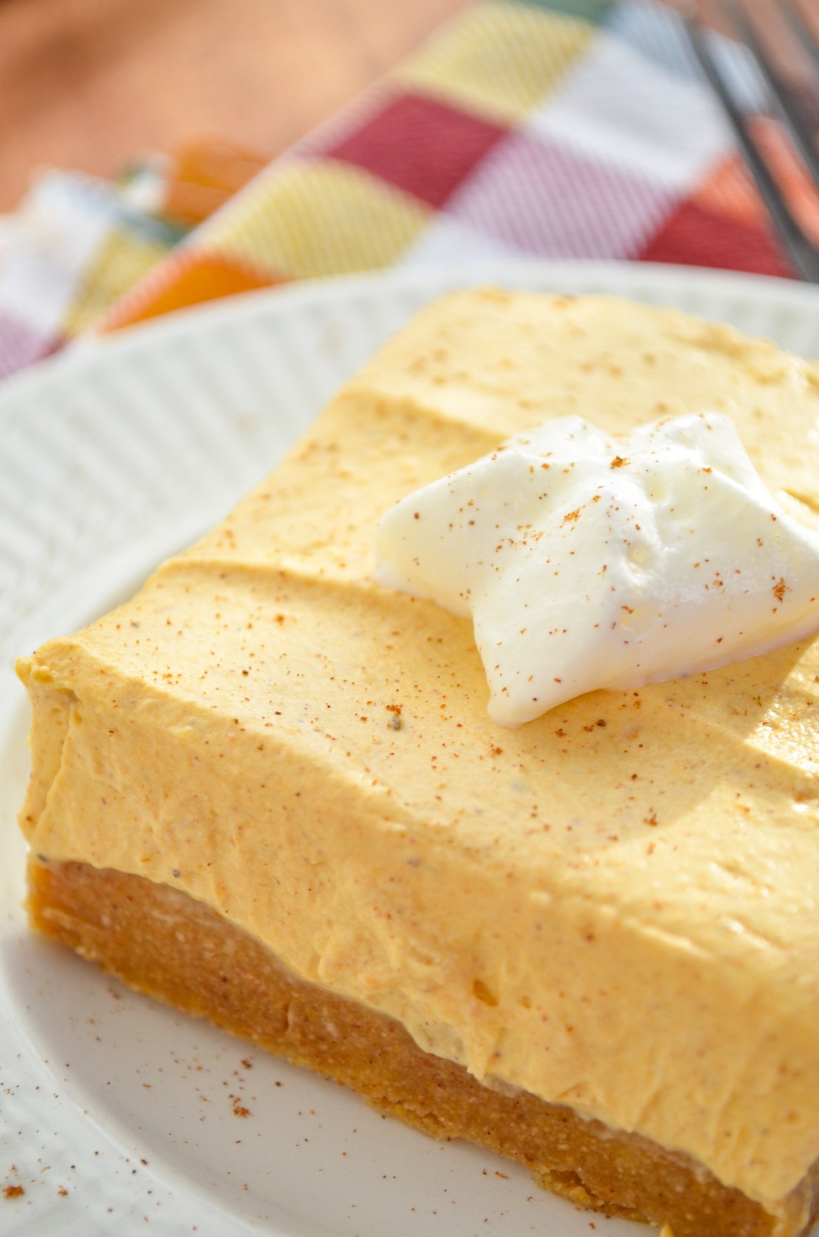 A single no bake pumpkin cheesecake bar, served with a dollop of whipped cream on top.