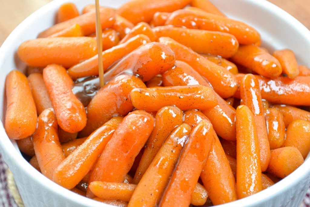 A thickened glaze being poured on top of a bowl of baby carrots.