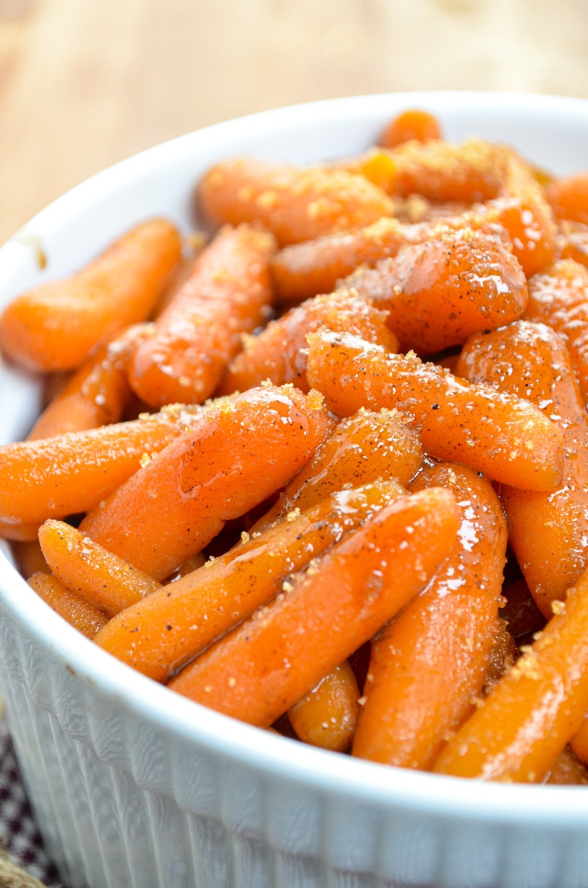 A white serving dish, filled with slow cooker maple carrots. Sprinkled with additional brown sugar.