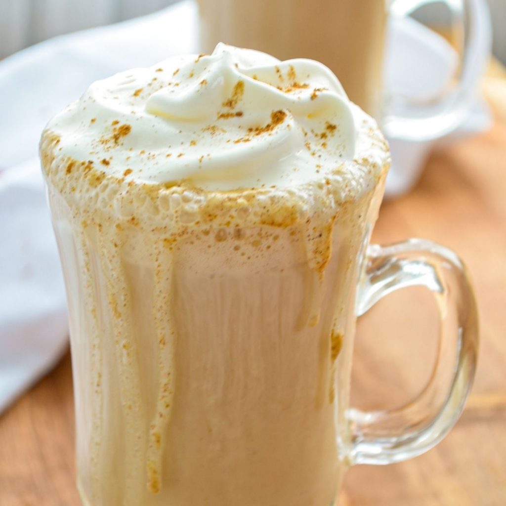 A glass mug filled with a pumpkin spice latte and covered with whipped cream.