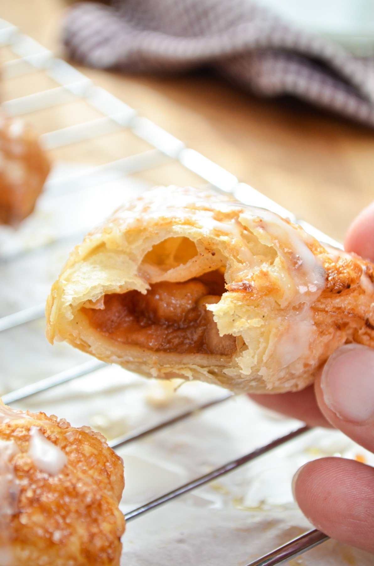 An apple turnover with a bite taken out of it, being placed on a wire rack.