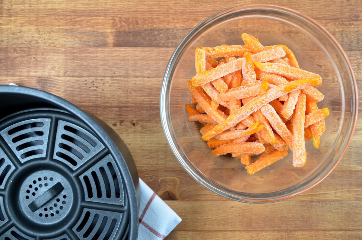 A bowl of frozen sweet potato fries and a basket style air fryer.