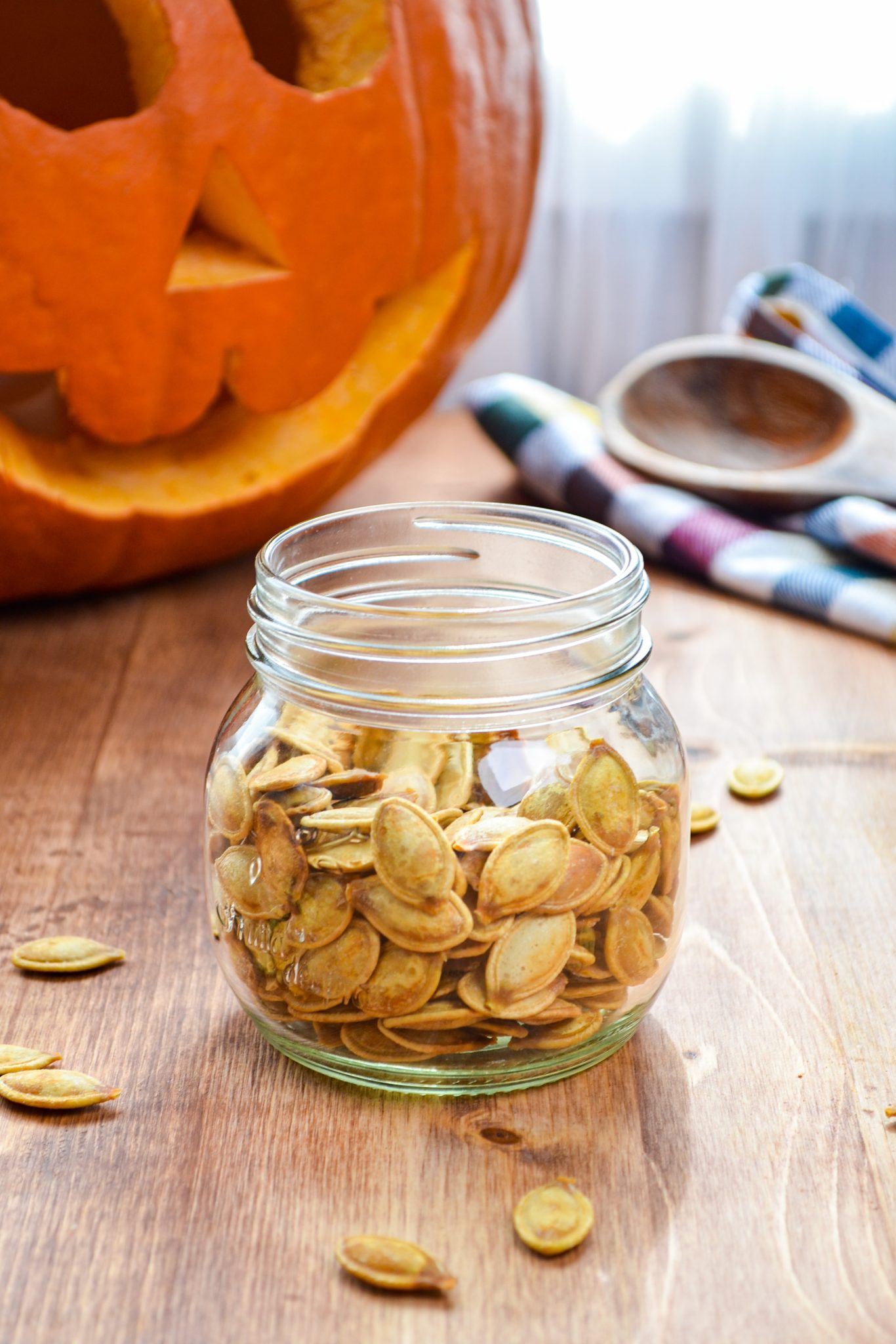 A jar of pumpkin seeds, with a large carved pumpkin in the background.
