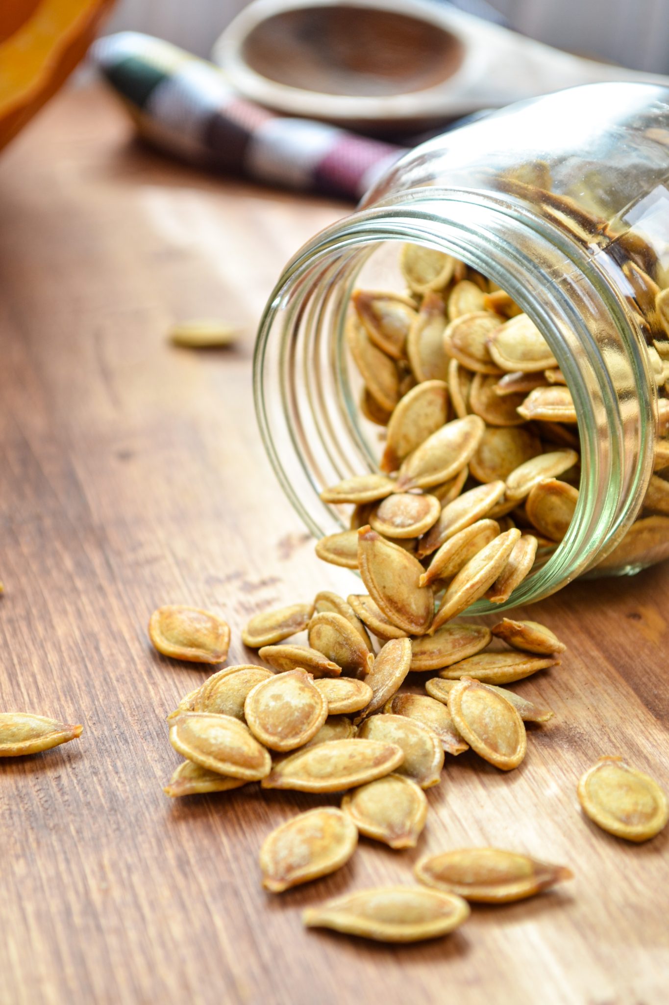 A jar of pumpkin seeds spilling onto a wood table.