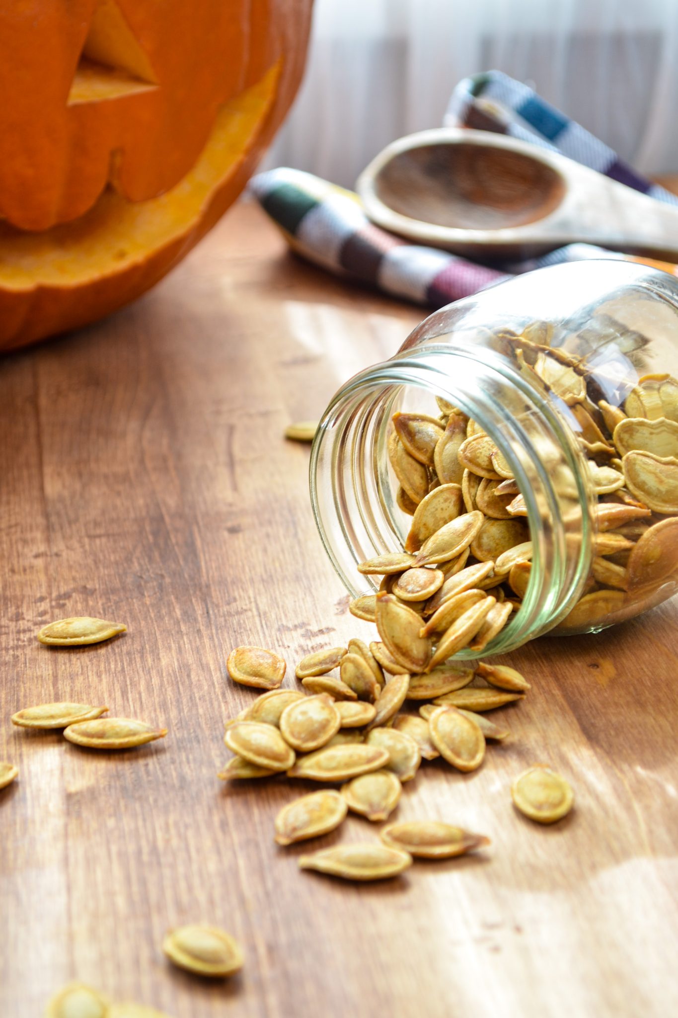 A jar of pumpkin seeds being spilled on the table, with a large pumpkin in the background.