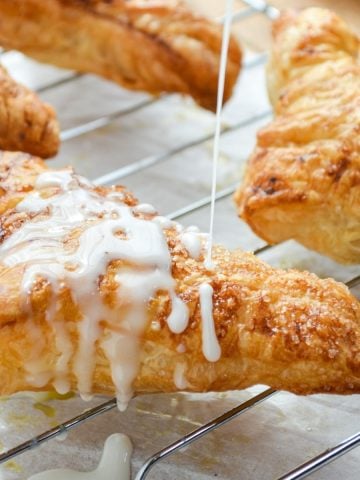 An apple turnover, being drizzled with a simple glaze.