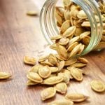 A jar of pumpkin seeds, spilled over onto a wood table.