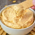 A serving bowl of pumpkin fluff dip, with a graham cracker being dipped in.
