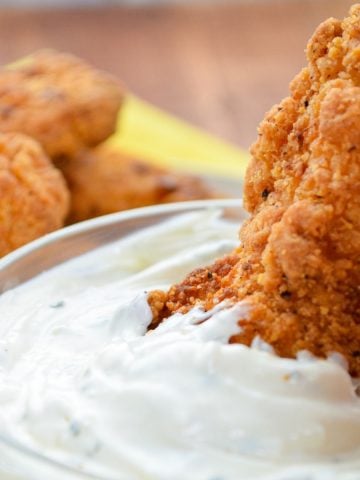 A fried chicken strip being dipped into ranch dip.