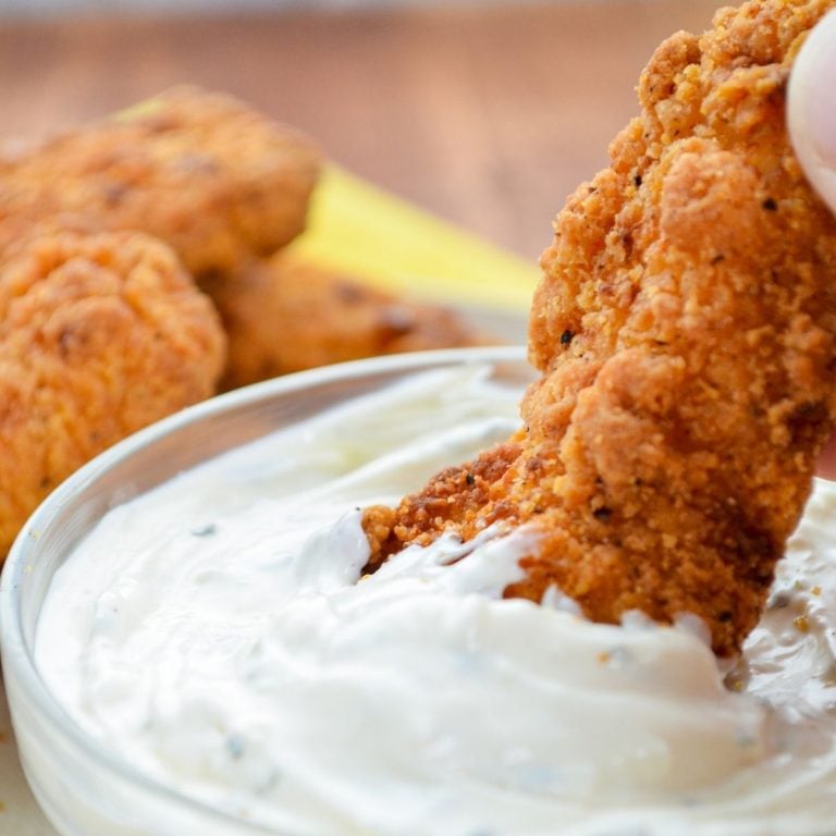 A fried chicken strip being dipped into ranch dip.