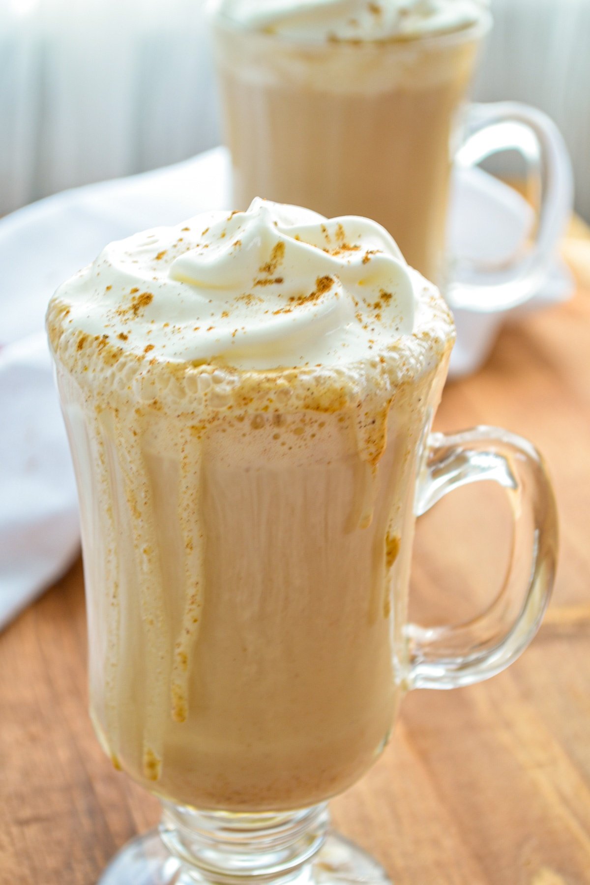 Two glasses of pumpkin spice lattes, topped with whipped cream.