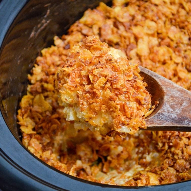 A large wooden spoon scoops up a portion of funeral potatoes made in a slow cooker.