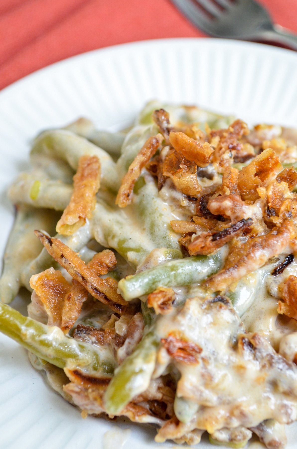A serving of green bean casserole on a white plate, topped with french fried onions.