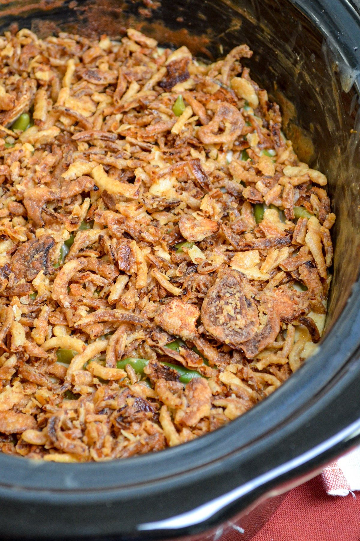 A slow cooker full of green bean casserole, topped with french fried onions.