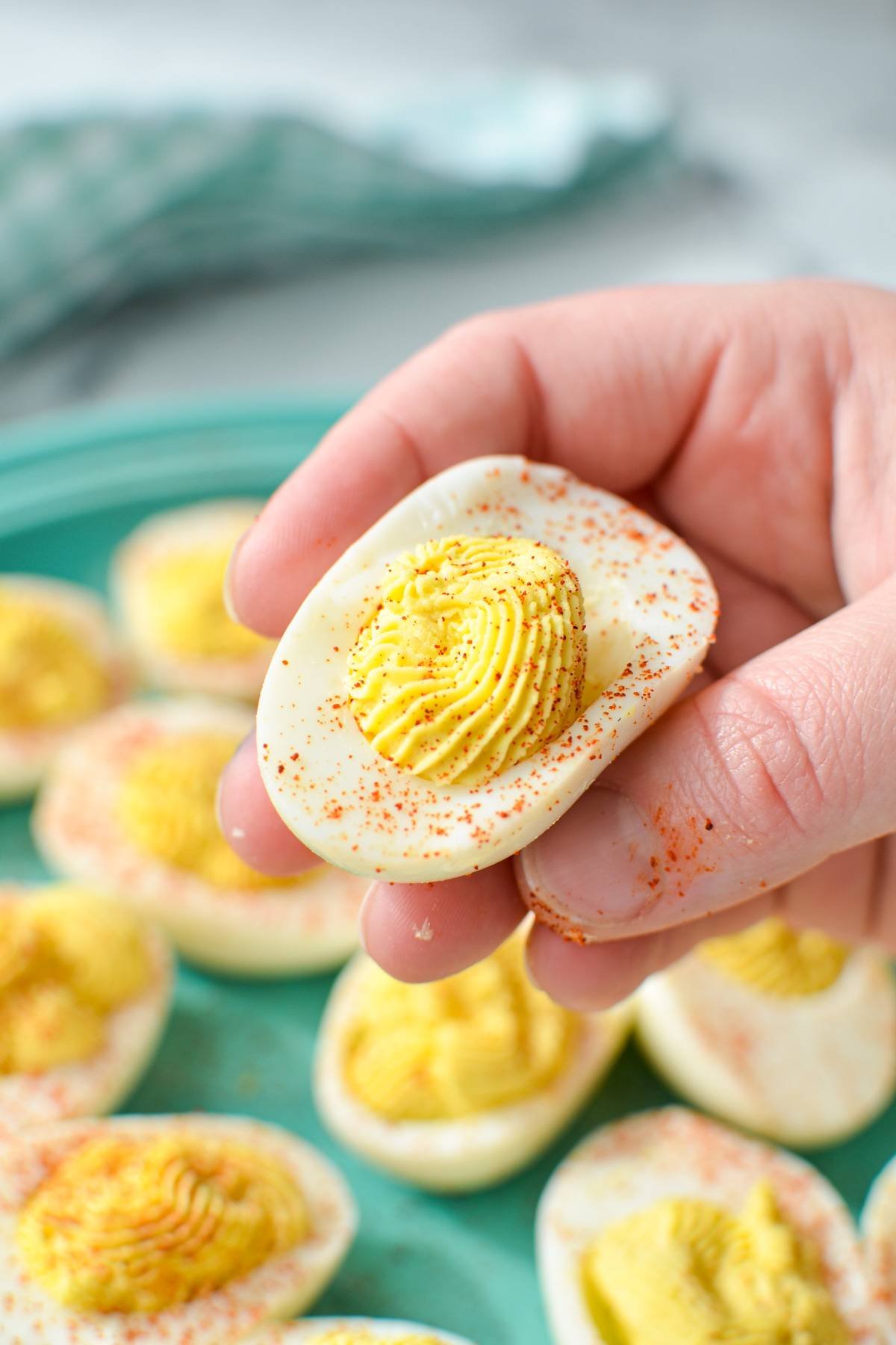 A hand holding a deviled egg, sprinkled with paprika
