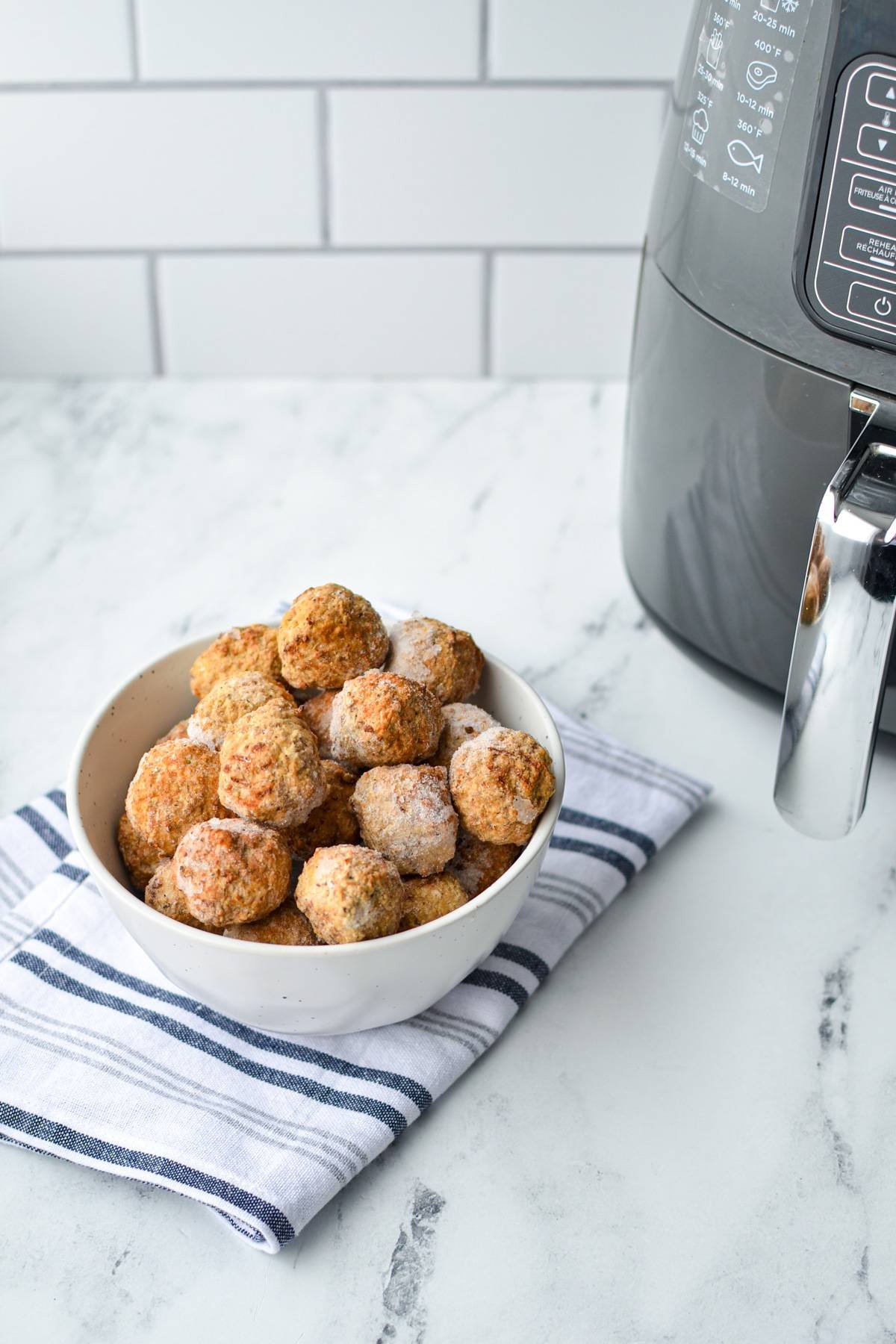 A bowl of frozen meatballs on a white and blue napkin, with an air fryer just out of view.