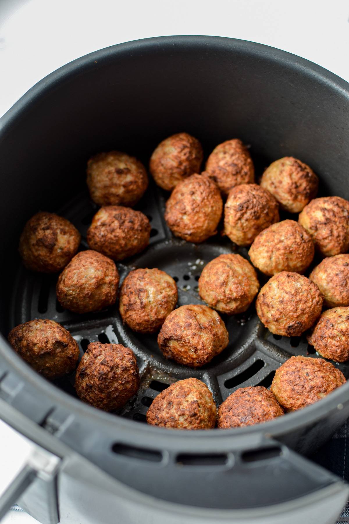 An air fryer basket filled with cooked meatballs.