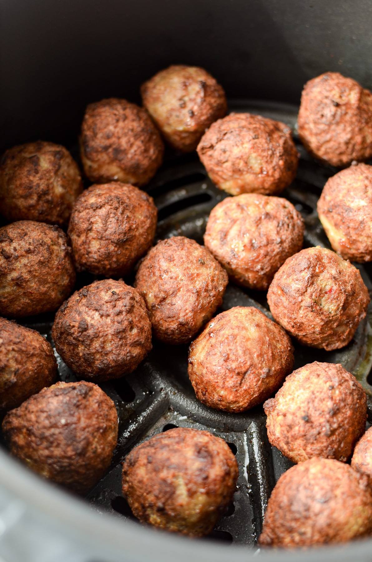 A close up of meatballs that have been cooked in an air fryer basket.