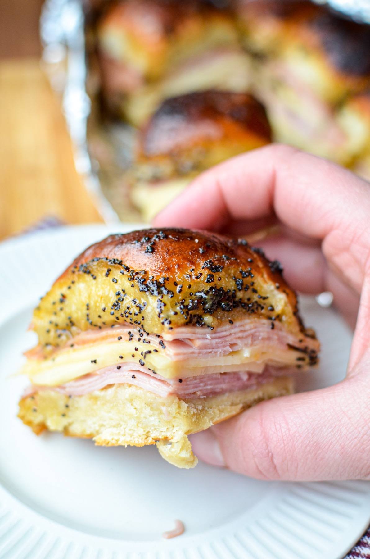 Holding a ham and cheese slider, covered with a poppy seed sauce.