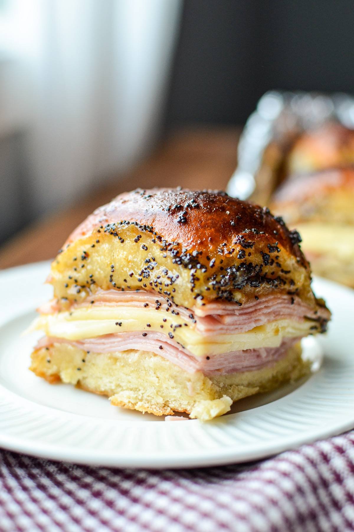 A single ham and cheese slider on a plate, covered in a poppy seed sauce.