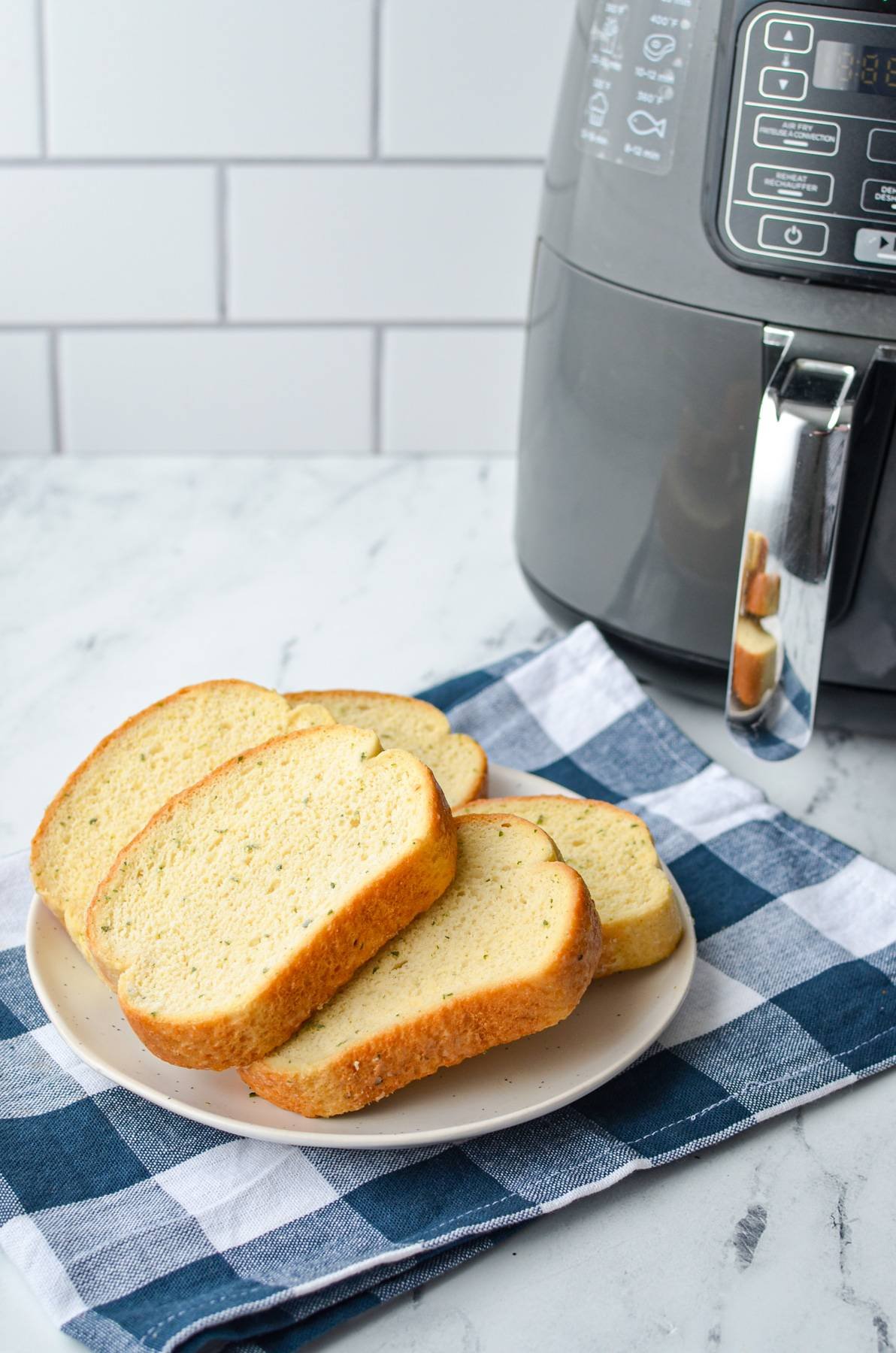 A plate of frozen garlic toast on a plate, next to a basket style air fryer.