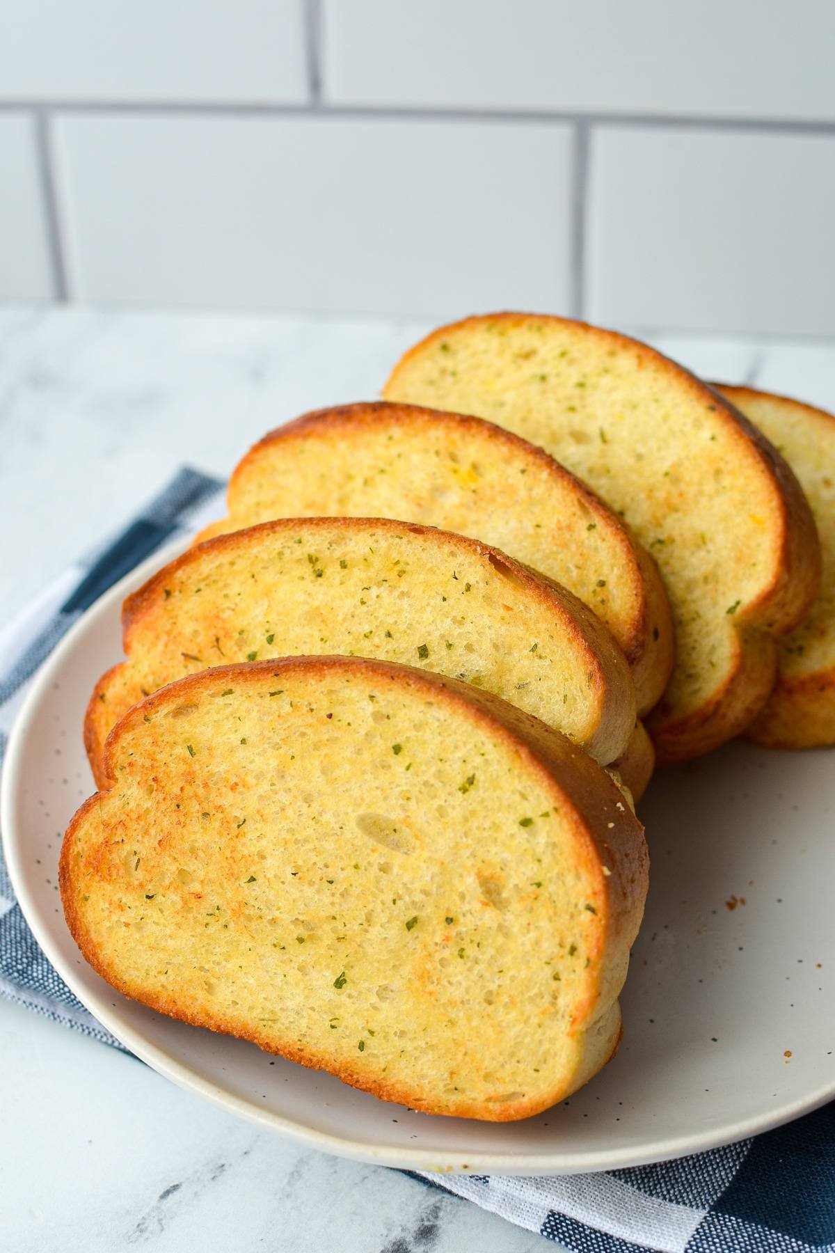 A plate of toasted garlic toast, resting on a blue check napkin.