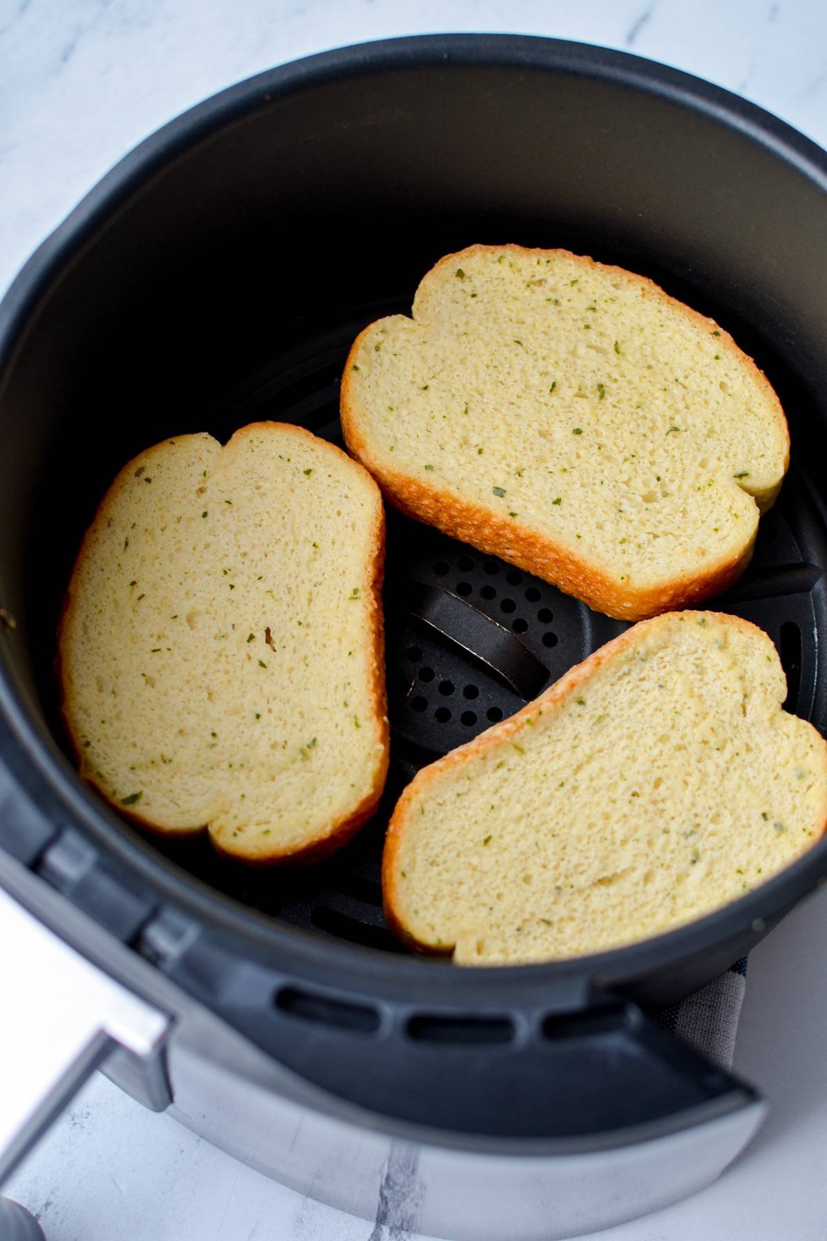 3 slices of garlic toast in the basket of an air fryer.