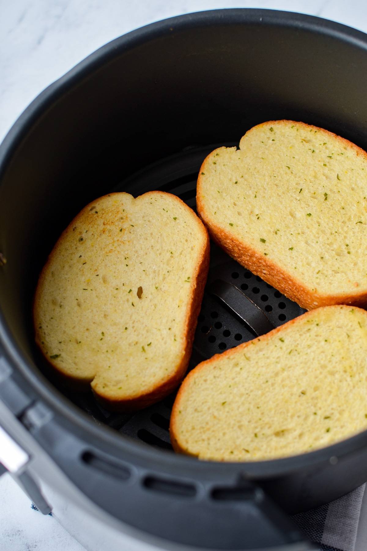 3 slices of lightly toasted garlic bread in the basket of an air fryer.