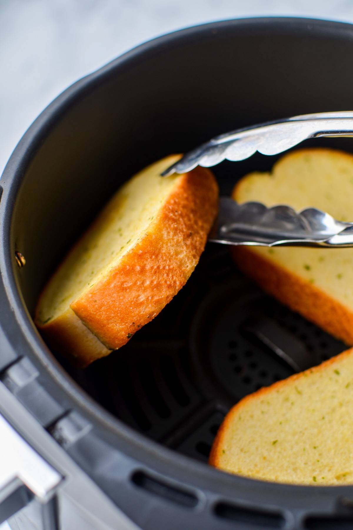 Flipping Texas Toast in an air fryer using a pair of tongs.