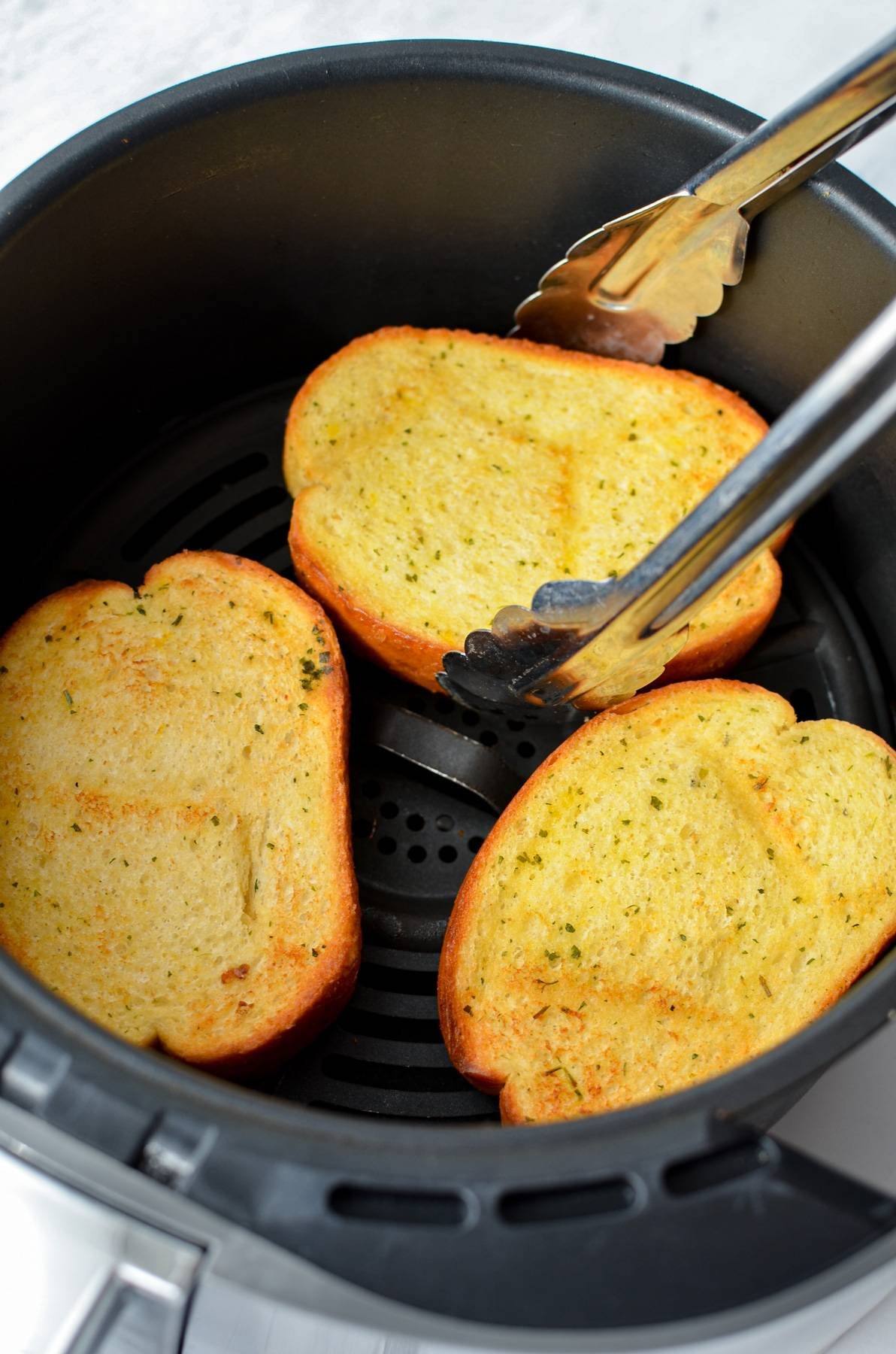 Removing a slice of frozen garlic bread from a cooking basket.