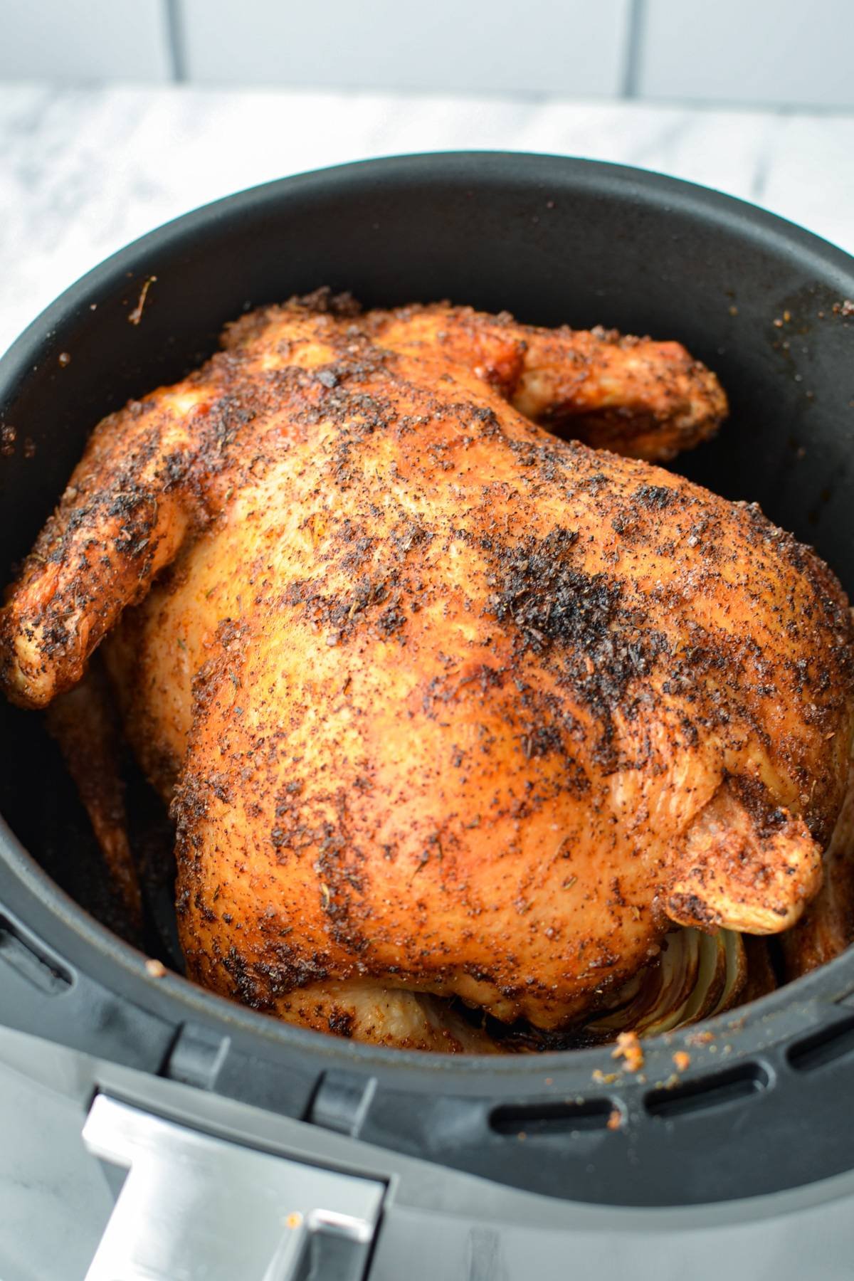 A whole chicken, breast side down, in an air fryer basket.
